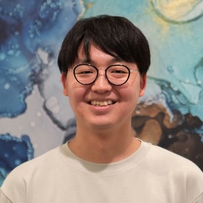 Portrait of a young man, grinning groadly, standing in front of a painting.