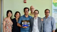 PhD student Tyler Knowlton smiling at the camera, surrounded by six members of his PhD committee, one joining remotely through an iPad